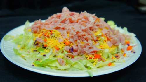 A plate of salad topped with shredded ham, cheese, and colorful vegetables on a bed of lettuce.