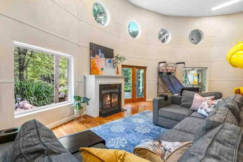 A modern circular living room with a fireplace, large windows, and a slide, featuring cozy gray sofas and a blue rug.