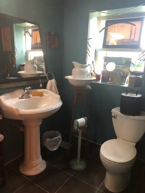 A small bathroom featuring a pedestal sink, toilet, and a window with decorative items.