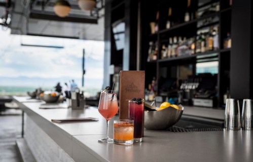 A stylish bar with colorful cocktails, a menu, and a scenic view in the background.