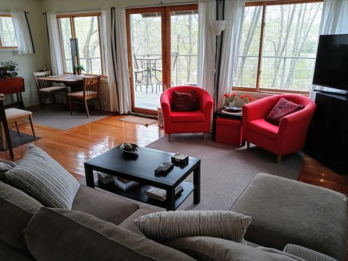 Cozy living room with a sofa, red chairs, a coffee table, and large windows overlooking a green outdoor view.