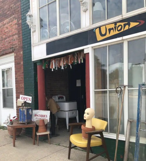A vintage shop entrance with a sign reading "Union," featuring antiques and a mannequin head on a chair outside.