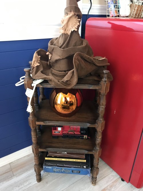 A wooden shelf with a sorting hat on top, a shiny orb, a toy train, and Harry Potter books.