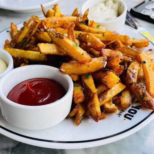 A plate of golden French fries served with ketchup and a creamy dipping sauce.