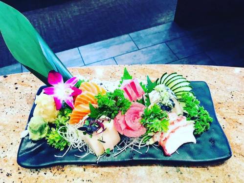 A beautifully arranged sushi platter featuring various sashimi, garnished with greens, wasabi, and a flower.