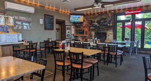Interior of a casual dining restaurant with empty tables, a fireplace, and a TV, featuring warm lighting and outdoor views.