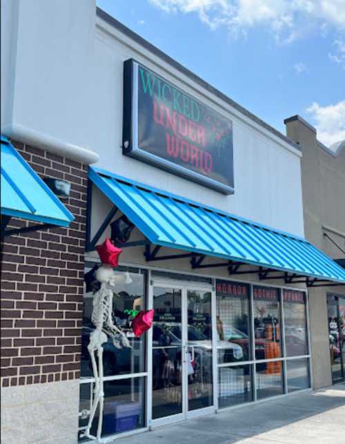 Storefront of "Wicked Underworld" featuring blue awnings, a skeleton decoration, and a sign for horror and gothic apparel.