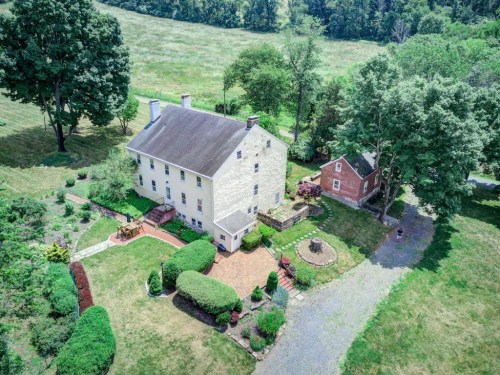 Aerial view of a large historic house with gardens, a patio, and a smaller building nearby, surrounded by greenery.