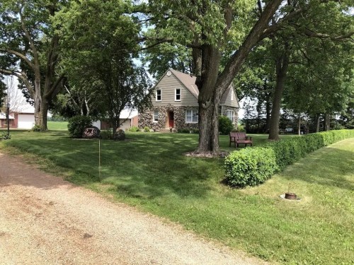 A charming house surrounded by trees and a well-maintained lawn, with a gravel path leading up to it.