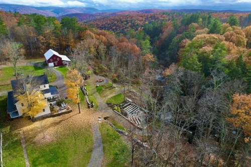 Aerial view of a scenic autumn landscape featuring a farmhouse, red barn, and colorful trees in the background.