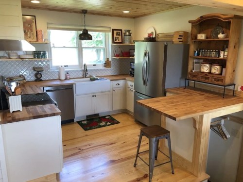 Bright kitchen with wooden accents, stainless steel appliances, and a cozy dining area featuring a small table and stool.