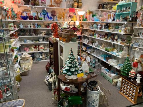 A cozy antique shop filled with various collectibles, glassware, and decorative items, including a small Christmas tree.