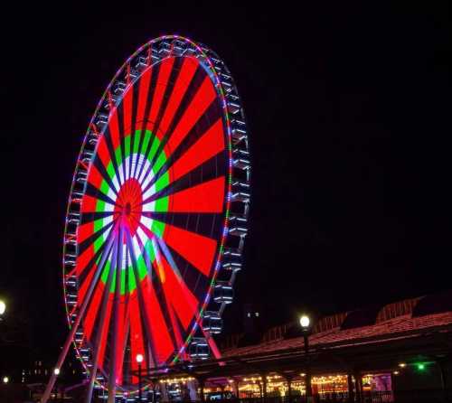 A brightly lit Ferris wheel at night, featuring vibrant red, green, and white patterns against a dark sky.