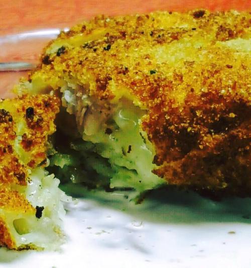 Close-up of a golden-brown, crispy fried cutlet with a flaky interior on a plate.