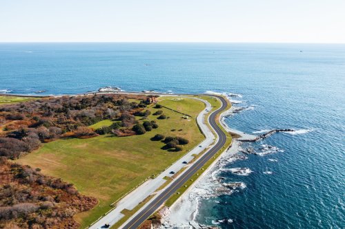 Aerial view of a coastal road winding along the shoreline, surrounded by green fields and blue ocean.