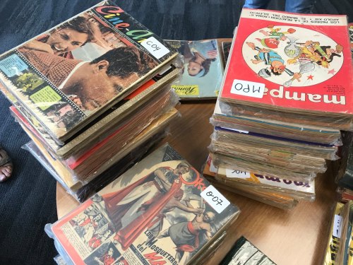 A stack of vintage magazines and comic books, some with colorful covers, arranged on a wooden table.