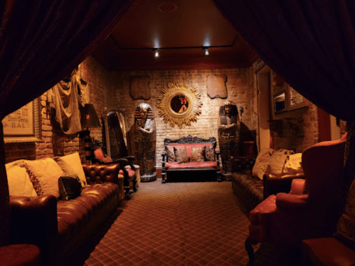 A dimly lit room with vintage furniture, including a sofa and armchairs, adorned with decorative elements and a mirror.