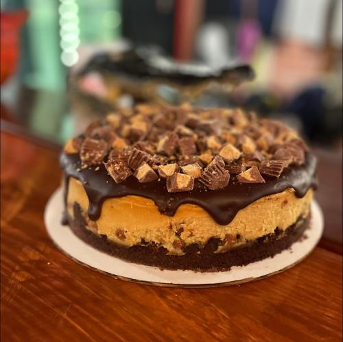 A decadent chocolate and peanut butter cheesecake topped with crushed candy pieces on a wooden table.