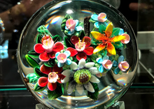 A glass paperweight featuring a colorful arrangement of various flowers, including red, blue, and yellow blooms.