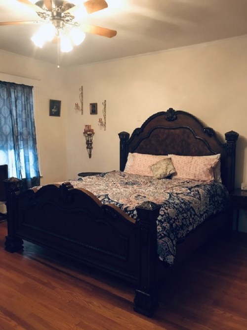 A cozy bedroom featuring a large wooden bed with a patterned blanket, a window with curtains, and wooden flooring.
