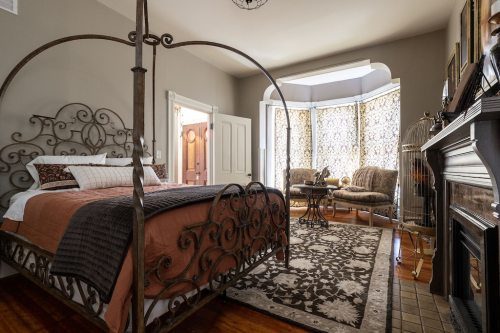 Cozy bedroom featuring an ornate metal bed, plush seating area, and decorative fireplace in a warm, inviting setting.