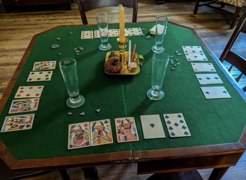 A green felt table set for a card game, featuring playing cards, glasses, and a candle in the center.