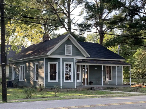 A charming blue house with a front porch, surrounded by trees and greenery on a quiet street.