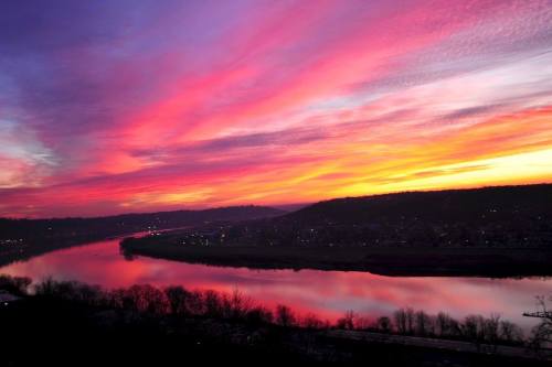 A vibrant sunset over a river, with colorful pink and purple clouds reflecting on the water's surface.