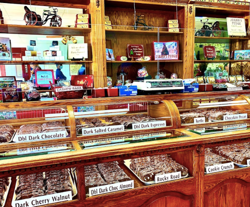 A display of various chocolates and candies in a vintage shop, featuring labeled trays of treats like dark chocolate and turtle.