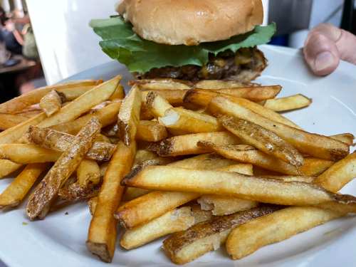 A plate of golden French fries beside a burger topped with lettuce and pickles on a soft bun.