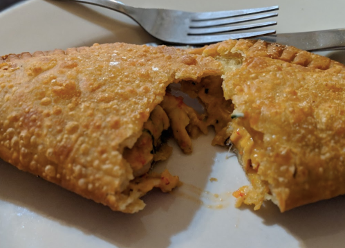 A golden, flaky pastry partially opened, revealing a savory filling inside, served on a white plate with a fork.