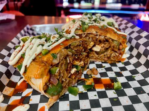 A close-up of a burrito cut in half, filled with rice, beans, and vegetables, drizzled with sauce and garnished.