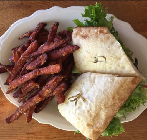 A plate with two halves of a sandwich and a side of crispy sweet potato fries, garnished with lettuce.