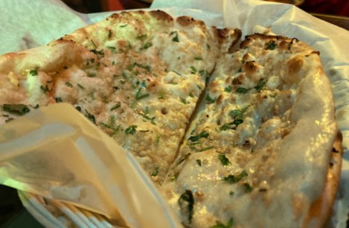 A basket of freshly baked naan bread, topped with herbs and lightly charred edges.