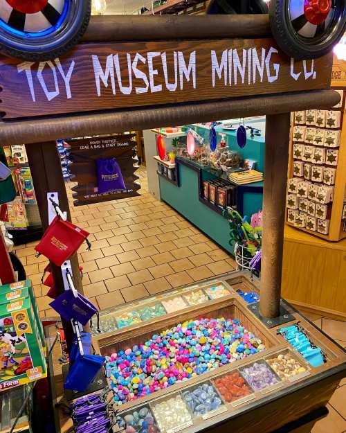 A colorful toy mining display with various small toys and gems in a wooden frame at a toy museum.