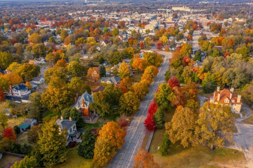 Aerial view of a colorful autumn landscape with trees in vibrant hues and a small town in the background.