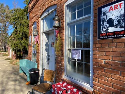 A brick building with a white door, lanterns, and art signs, featuring a bench and chairs outside.