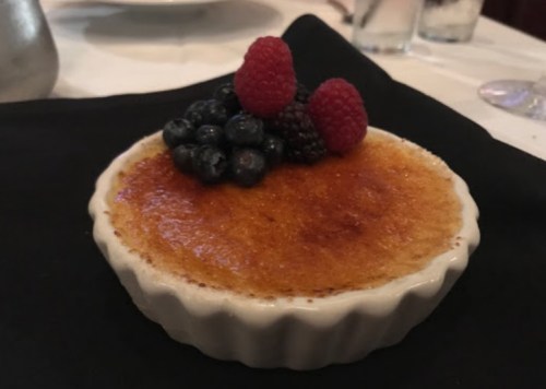 A creamy dessert topped with fresh raspberries and blueberries, served in a white ramekin on a black napkin.