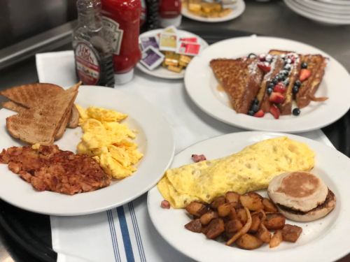 A breakfast spread featuring scrambled eggs, hash browns, an omelet, toast, and French toast with fruit.
