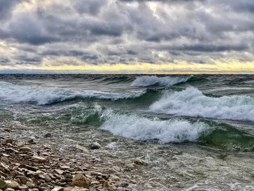 Waves crash on a rocky shore under a cloudy sky, with hints of sunset in the background.