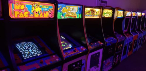 A row of classic arcade game machines, including Ms. Pac-Man, illuminated with colorful neon lights.