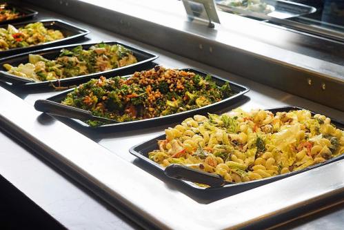 A variety of colorful salads and pasta dishes displayed in black trays on a buffet counter.