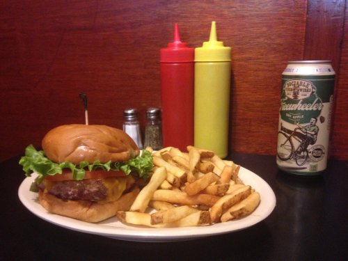 A cheeseburger with lettuce on a plate, served with fries, ketchup, mustard, and a can of apple soda.