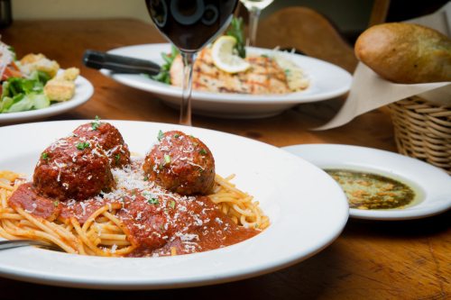 A plate of spaghetti with meatballs and marinara sauce, garnished with parsley and Parmesan, with salad and bread in the background.