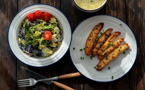 A colorful meal featuring a salad with cherry tomatoes and a side of crispy breadsticks on a wooden table.