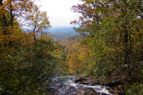 A scenic view of a valley with colorful autumn foliage and a small waterfall in the foreground.
