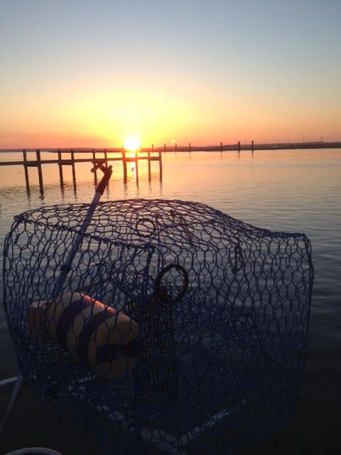 A fishing net rests on a boat, with a vibrant sunset reflecting on calm waters and a pier in the background.