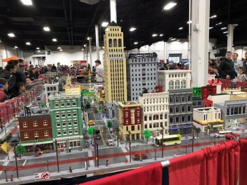A detailed LEGO city display with buildings, streets, and miniature figures, set up at a crowded exhibition.