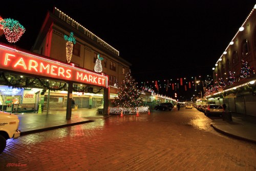 A festive night scene of a farmers market, adorned with colorful lights and a decorated Christmas tree.