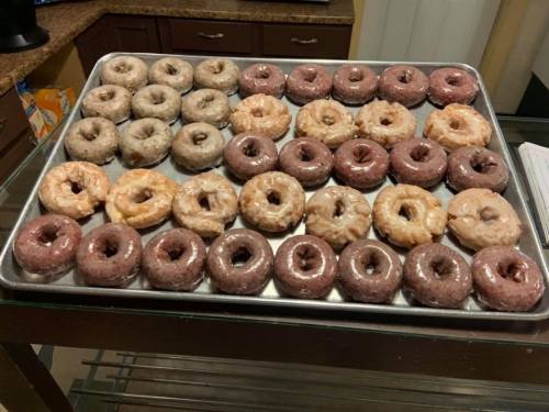A tray of assorted donuts, featuring glazed, chocolate, and powdered varieties, neatly arranged in rows.